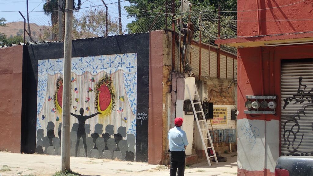 man looking at construction next to a mural of a man with outstretched arms holding two hearts.