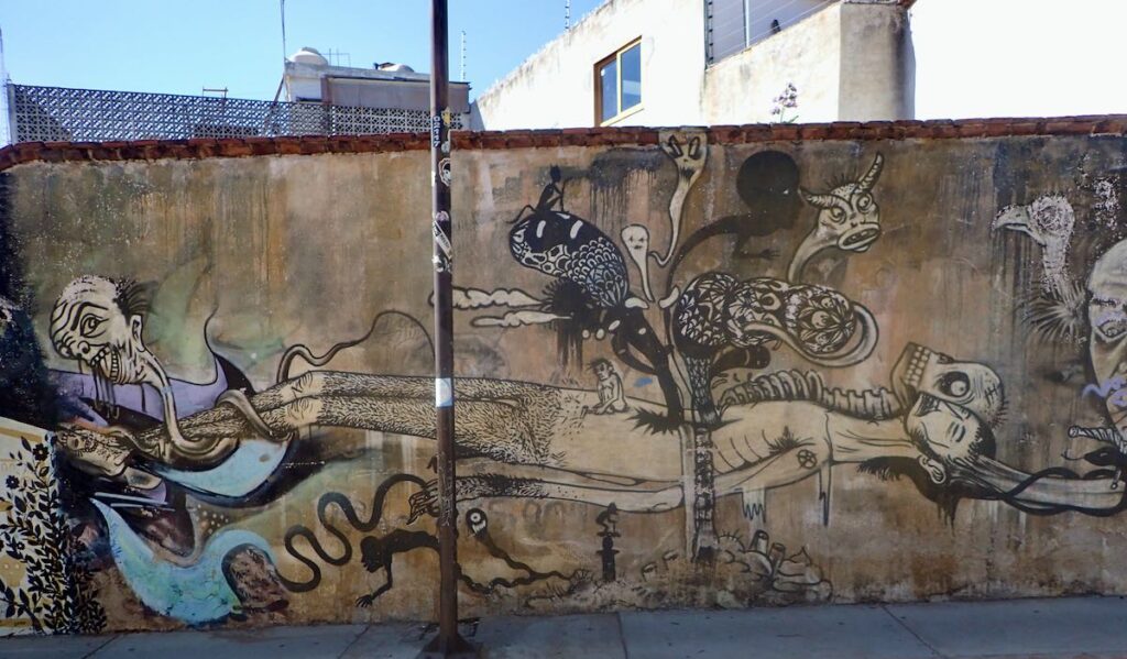 mural of man/skeleton with monsters and ghosts coming out of a hole in his stomach and a strange demon-like head wrapped around his legs.